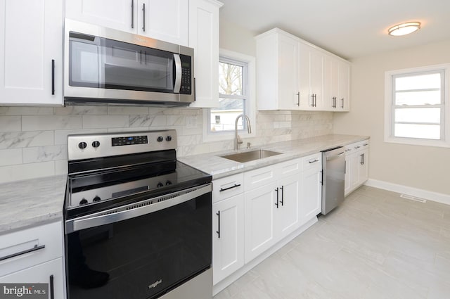 kitchen with light stone countertops, stainless steel appliances, white cabinetry, sink, and tasteful backsplash