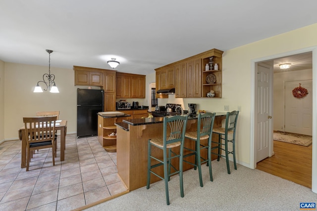 kitchen featuring pendant lighting, a kitchen bar, kitchen peninsula, a chandelier, and black refrigerator