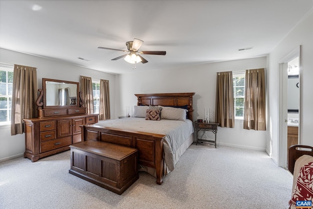 carpeted bedroom featuring multiple windows, ceiling fan, and ensuite bath