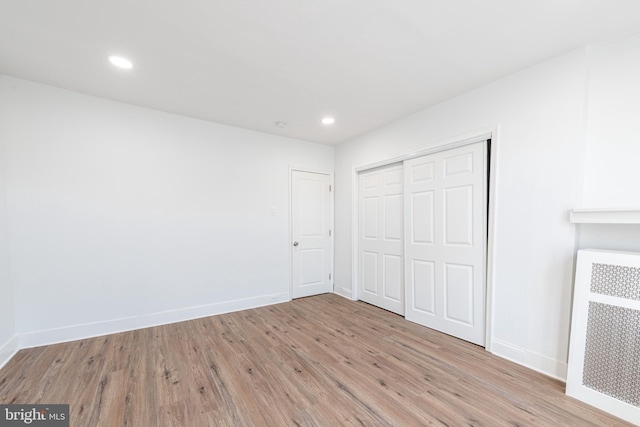 unfurnished bedroom with light hardwood / wood-style flooring, radiator heating unit, and a closet