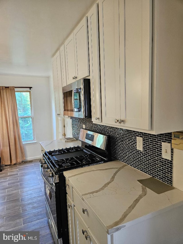 kitchen featuring white cabinetry, light stone counters, decorative backsplash, appliances with stainless steel finishes, and hardwood / wood-style flooring