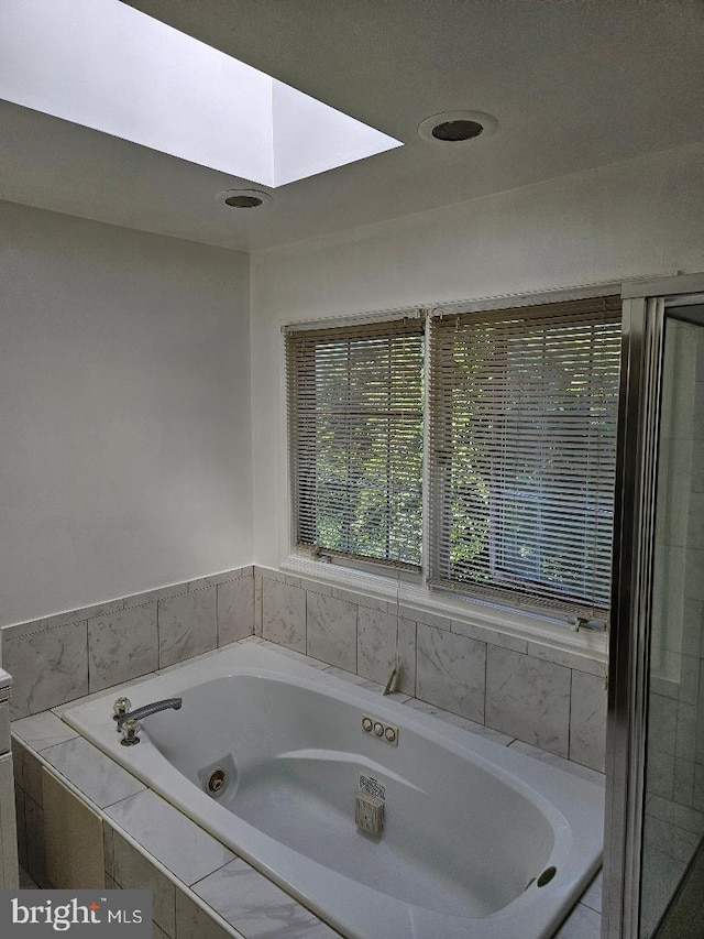 bathroom featuring a skylight and tiled bath