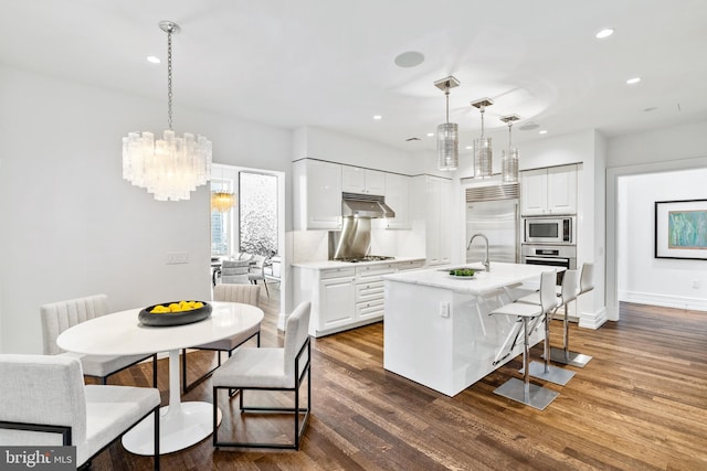 kitchen featuring white cabinets, dark hardwood / wood-style flooring, built in appliances, and hanging light fixtures