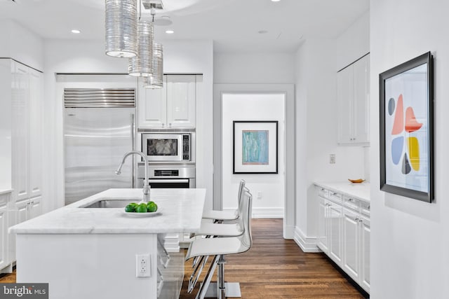 kitchen with built in appliances, white cabinetry, an island with sink, and pendant lighting