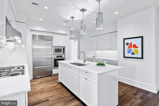 kitchen with built in appliances, white cabinets, sink, and an island with sink