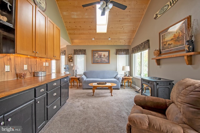 living area with ceiling fan, light colored carpet, wooden ceiling, a wood stove, and high vaulted ceiling