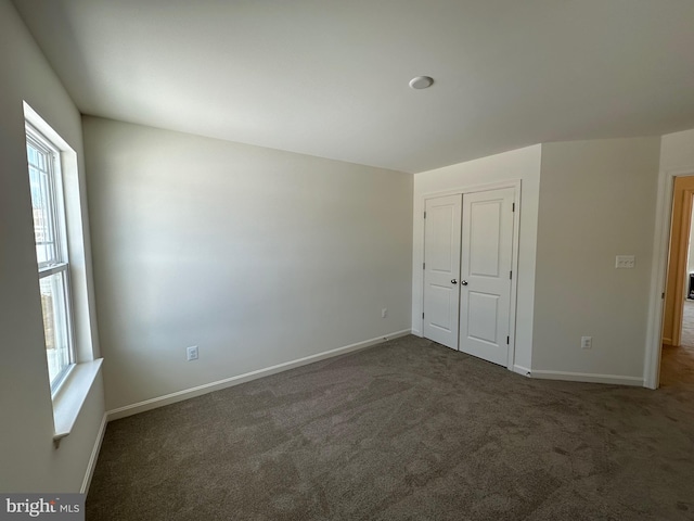 unfurnished bedroom with multiple windows, dark colored carpet, and a closet