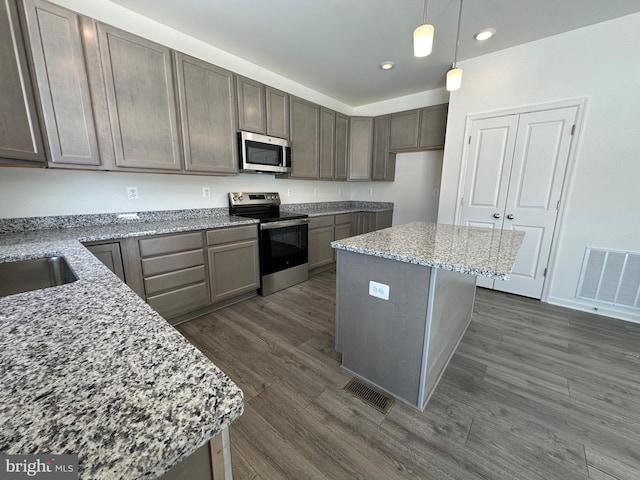 kitchen with stainless steel appliances, a kitchen island, light stone counters, and decorative light fixtures