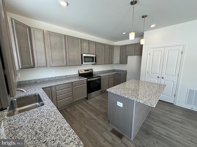 kitchen featuring sink, hanging light fixtures, a kitchen island, stainless steel appliances, and light stone countertops