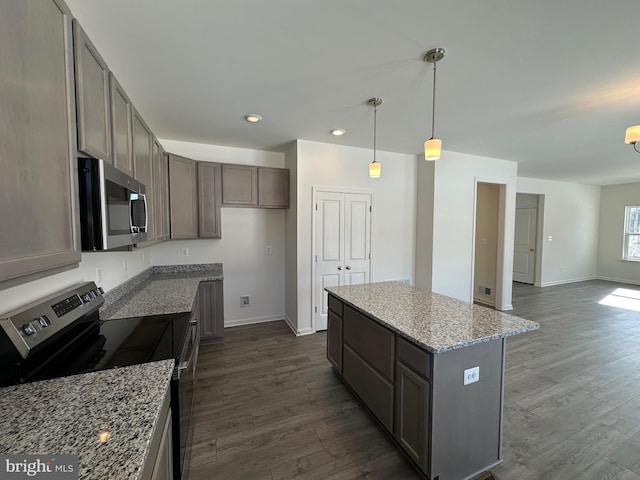 kitchen featuring appliances with stainless steel finishes, hanging light fixtures, dark hardwood / wood-style floors, a center island, and light stone countertops