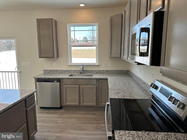 kitchen featuring light stone counters, appliances with stainless steel finishes, sink, and light hardwood / wood-style flooring