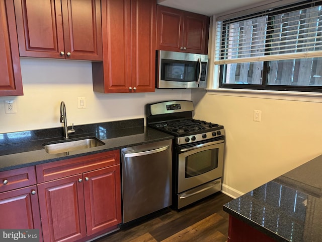 kitchen with dark wood-type flooring, dark stone counters, appliances with stainless steel finishes, and sink