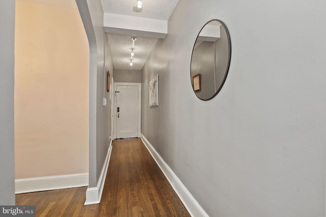 hall with dark wood-type flooring, track lighting, and a textured ceiling