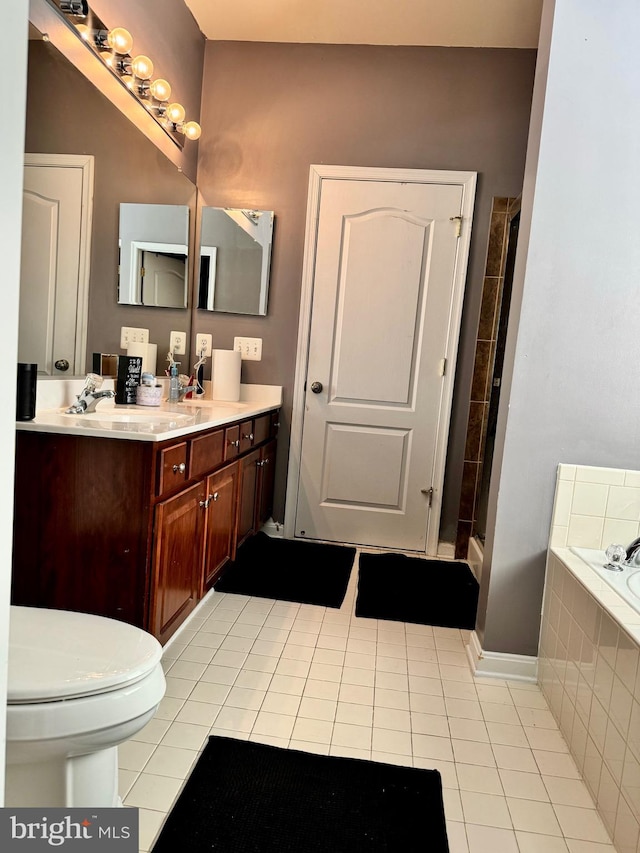 bathroom featuring tile patterned flooring, vanity, tiled bath, and toilet