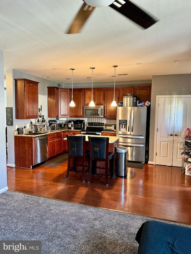 kitchen with a kitchen bar, stainless steel appliances, a kitchen island, ceiling fan, and dark hardwood / wood-style floors