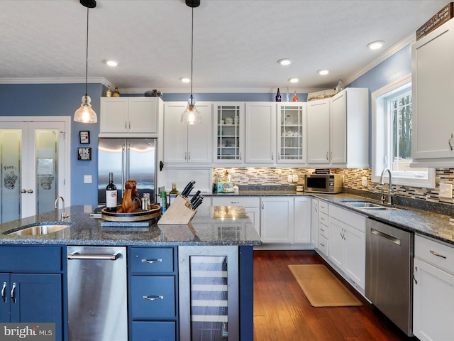 kitchen with sink, appliances with stainless steel finishes, white cabinets, a kitchen island, and decorative light fixtures