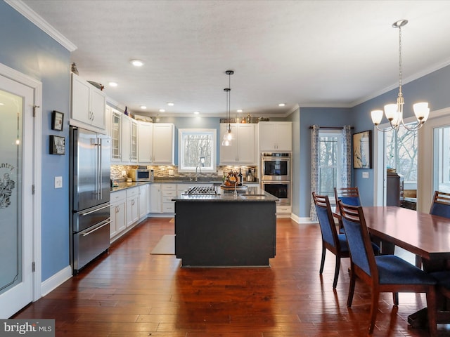 kitchen with white cabinetry, hanging light fixtures, a kitchen island, stainless steel appliances, and decorative backsplash