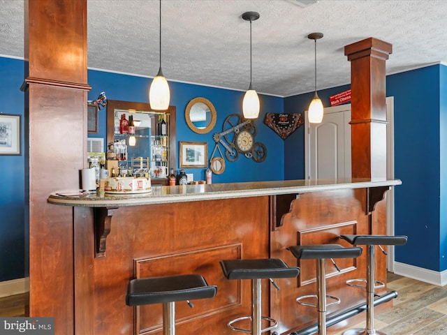 bar featuring pendant lighting, hardwood / wood-style flooring, decorative columns, and a textured ceiling