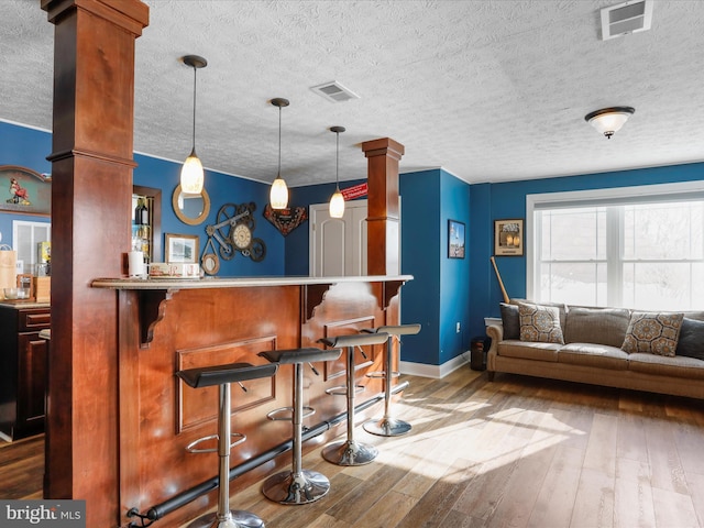 bar featuring hardwood / wood-style flooring, pendant lighting, a textured ceiling, and ornate columns