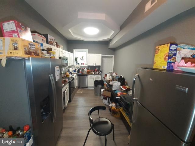 kitchen featuring dark hardwood / wood-style flooring, stainless steel appliances, a tray ceiling, and white cabinetry