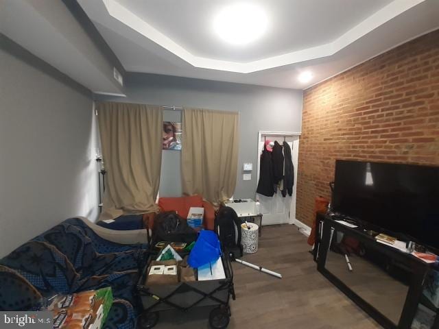 living room featuring hardwood / wood-style flooring, a raised ceiling, and brick wall