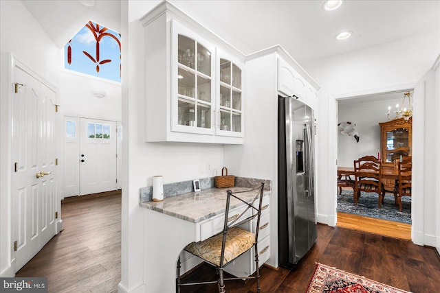 kitchen featuring white cabinets, light stone countertops, a notable chandelier, stainless steel fridge, and dark wood-type flooring