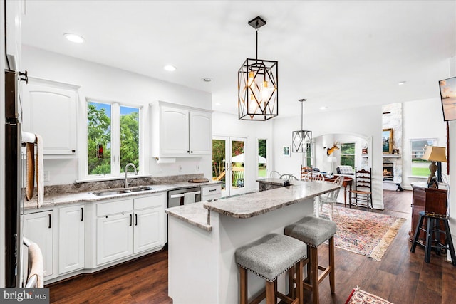 kitchen featuring decorative light fixtures, light stone counters, sink, dark hardwood / wood-style floors, and an island with sink