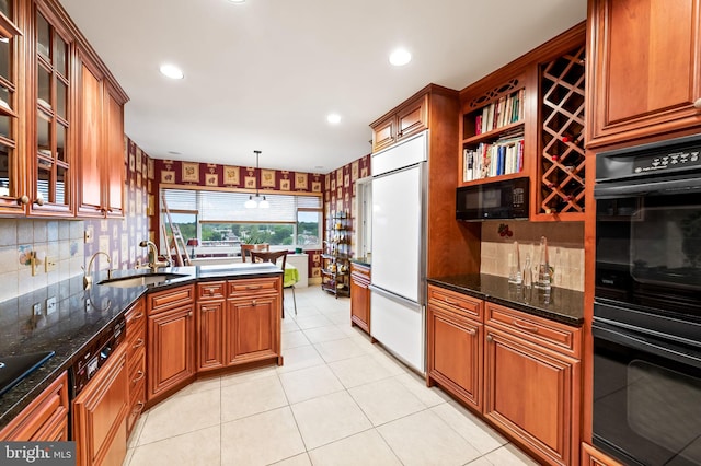 kitchen featuring brown cabinetry, dark stone countertops, a sink, and black appliances