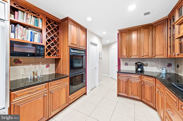 kitchen with black appliances, visible vents, brown cabinetry, and dark stone countertops