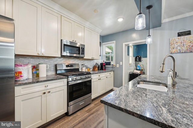 kitchen with appliances with stainless steel finishes, hanging light fixtures, dark stone countertops, ornamental molding, and sink