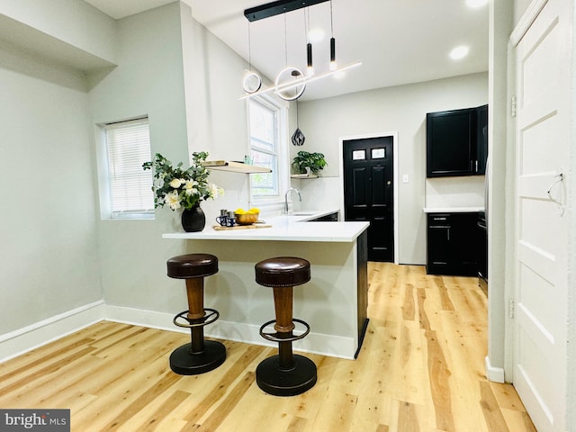 kitchen with sink, hanging light fixtures, light wood-type flooring, a kitchen bar, and kitchen peninsula