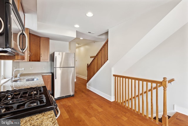 kitchen featuring black microwave, gas range, freestanding refrigerator, brown cabinetry, and a sink