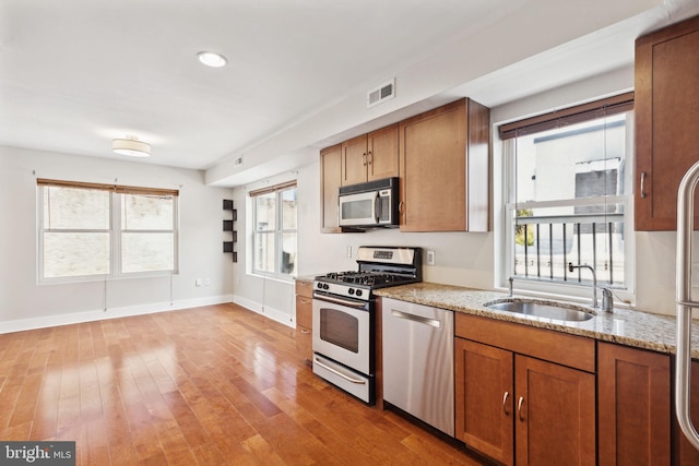 kitchen featuring light stone counters, visible vents, a sink, stainless steel appliances, and light wood-style floors