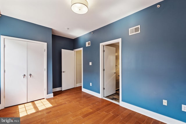 unfurnished bedroom with baseboards, a closet, visible vents, and wood finished floors