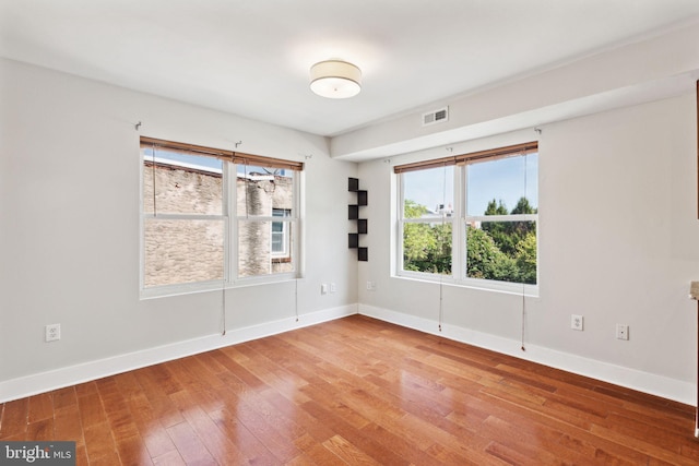 empty room with visible vents, wood-type flooring, and baseboards