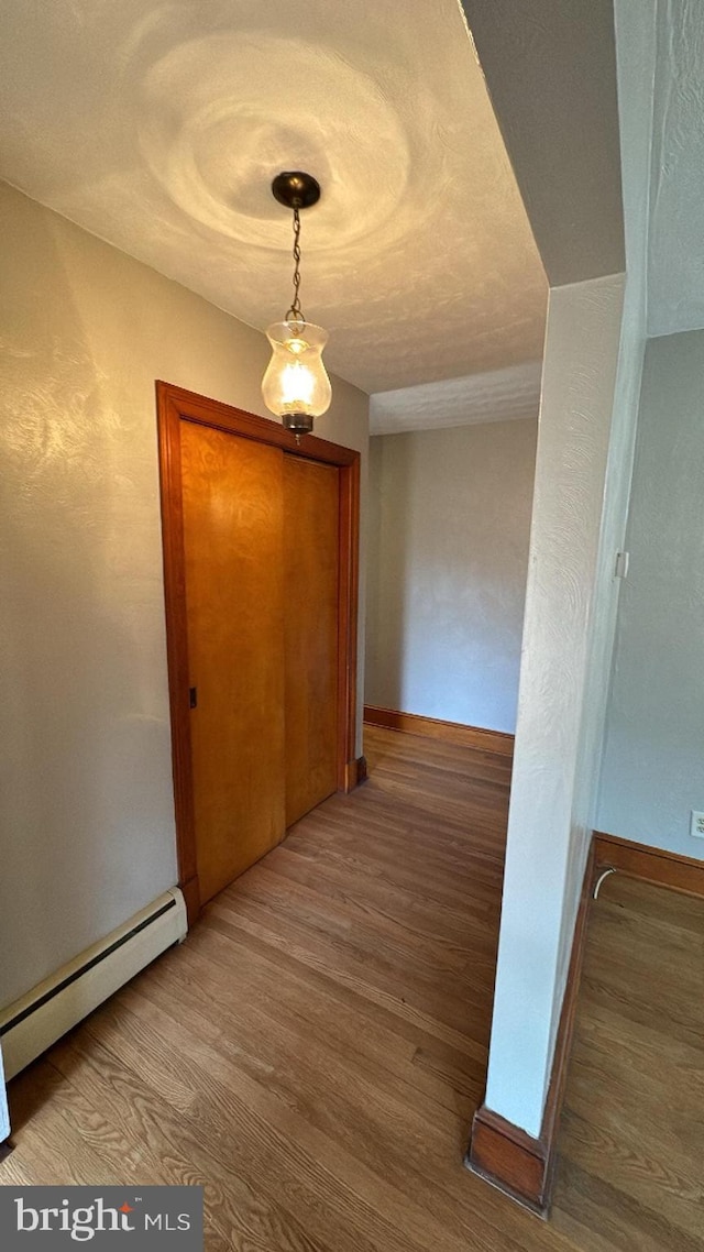 hallway with a baseboard radiator, baseboards, and wood finished floors