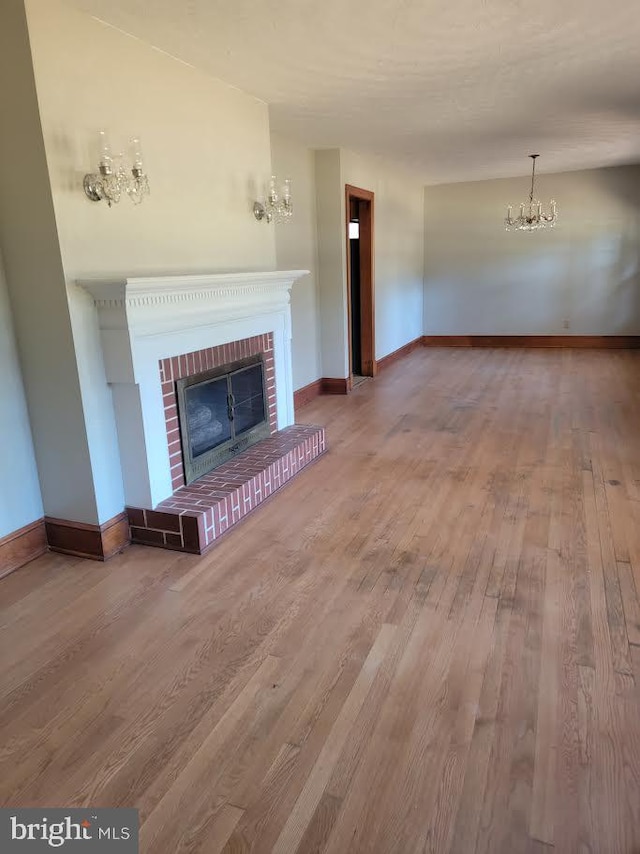 unfurnished living room featuring a brick fireplace, a notable chandelier, baseboards, and wood finished floors