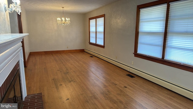 unfurnished dining area with hardwood / wood-style floors, a baseboard radiator, a chandelier, a fireplace, and a textured ceiling