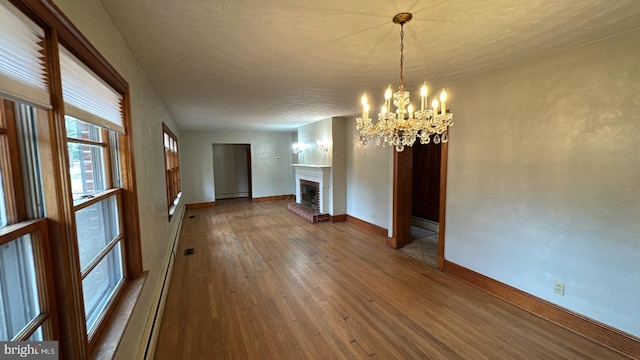 unfurnished living room featuring a chandelier, a baseboard radiator, a fireplace, wood finished floors, and baseboards