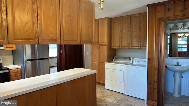 kitchen with light tile patterned floors, washer and clothes dryer, brown cabinets, stainless steel appliances, and light countertops