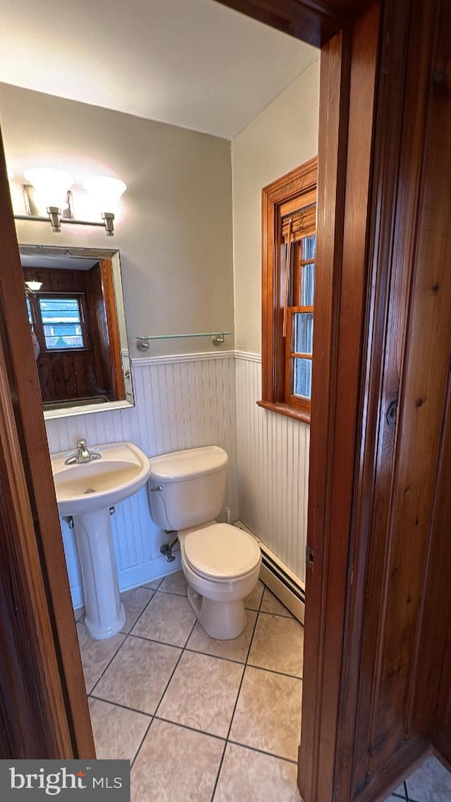 half bath featuring toilet, a wainscoted wall, a sink, baseboard heating, and tile patterned floors