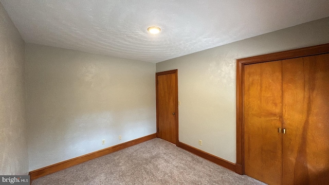 unfurnished bedroom featuring a closet, a textured ceiling, and light colored carpet