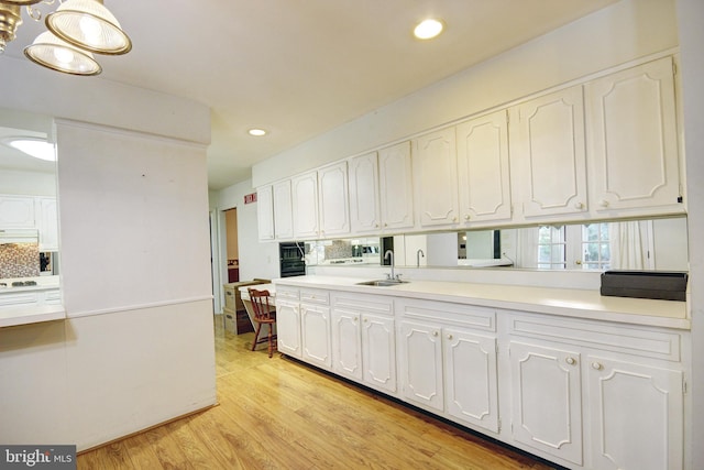 kitchen featuring pendant lighting, sink, tasteful backsplash, white cabinetry, and light hardwood / wood-style flooring