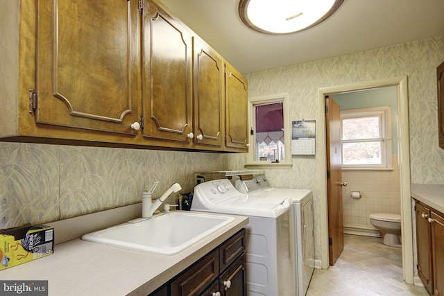 clothes washing area featuring tile walls, washing machine and dryer, cabinets, and sink