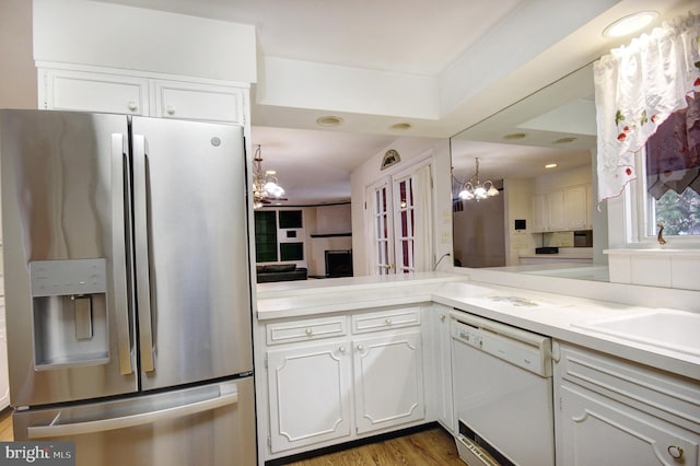 kitchen with dark hardwood / wood-style flooring, dishwasher, kitchen peninsula, white cabinets, and stainless steel fridge