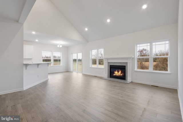 unfurnished living room featuring baseboards, light wood-type flooring, recessed lighting, a glass covered fireplace, and high vaulted ceiling