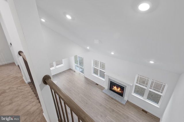 living area featuring visible vents, a glass covered fireplace, wood finished floors, recessed lighting, and lofted ceiling