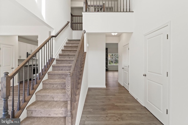 stairway with hardwood / wood-style floors and a towering ceiling