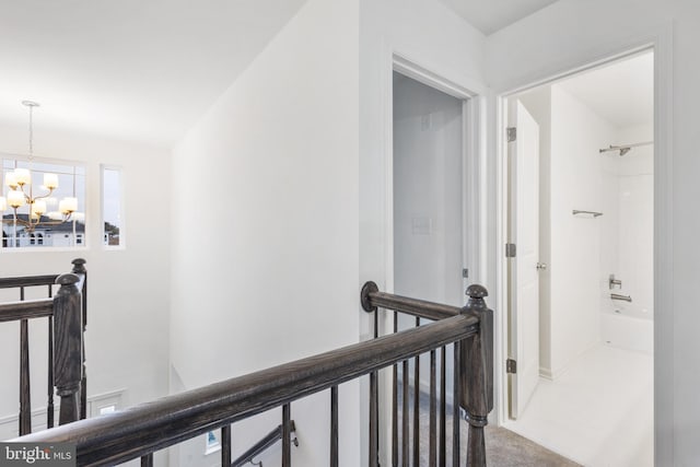 corridor with an upstairs landing, carpet flooring, and an inviting chandelier