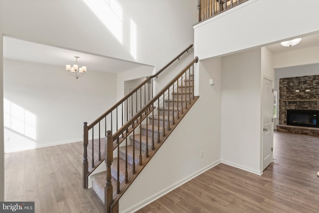 stairway featuring a fireplace, wood-type flooring, a towering ceiling, and a notable chandelier